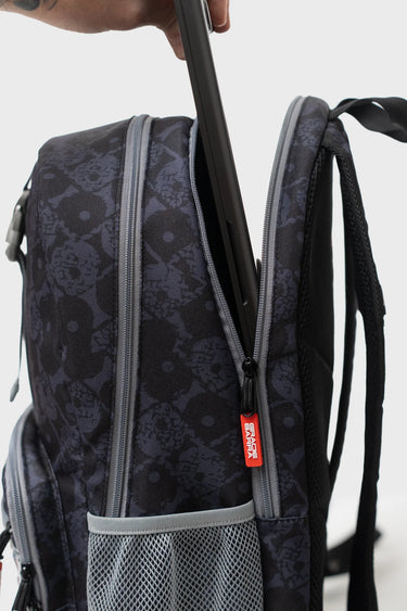 Hand sliding a laptop into the padded laptop sleeve of the black Barra Beachwalk Backpack, with a red Gracie Barra zipper pull and gray mesh side pocket.