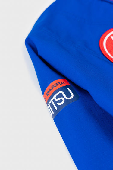Close-up of the kimono sleeve with woven Gracie Barra Jiu-Jitsu label and red round patch on blue ripstop fabric