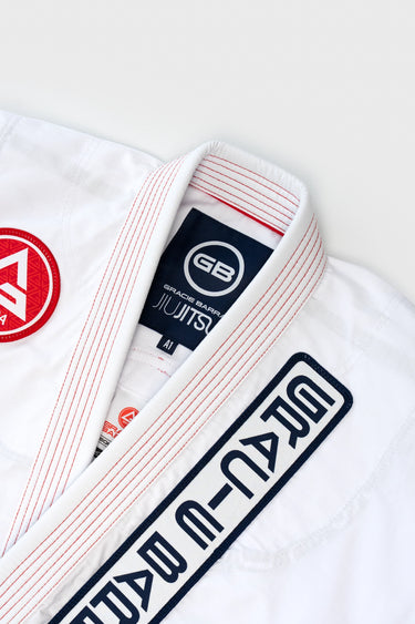 Close-up of the white ripstop kimono collar and lapel, showing red contrast stitching, the navy GB Gracie Barra Jiu-Jitsu woven neck label and embroidered chest patch